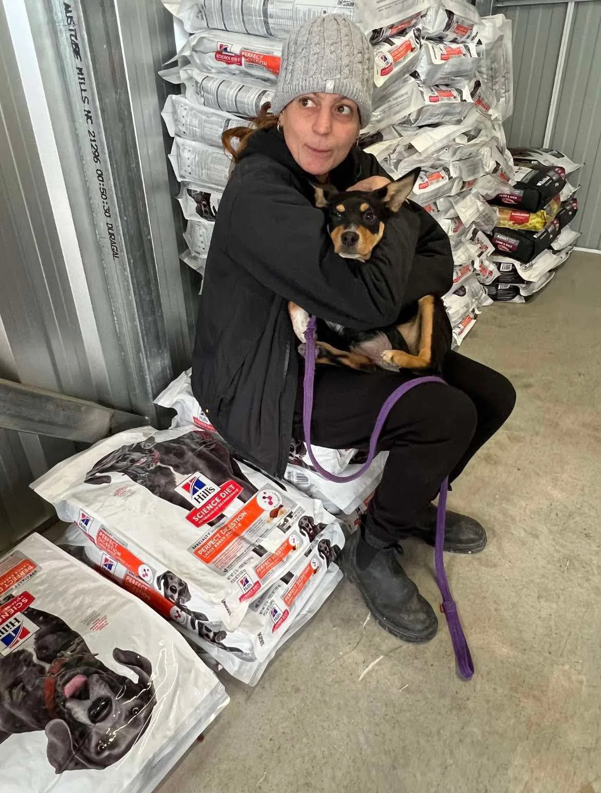 A person holding a dog beside donated supplies