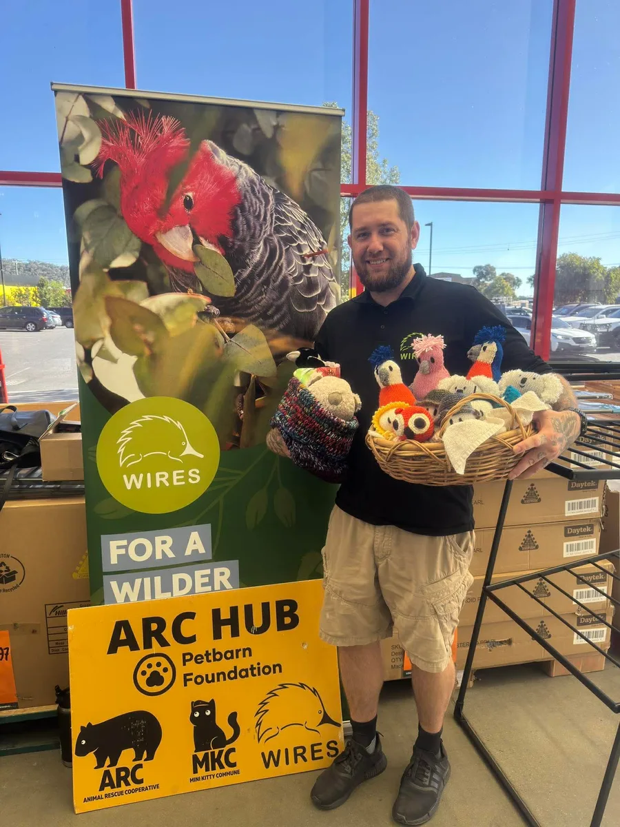 A volunteer holding colourful handmade items beside an ARC display